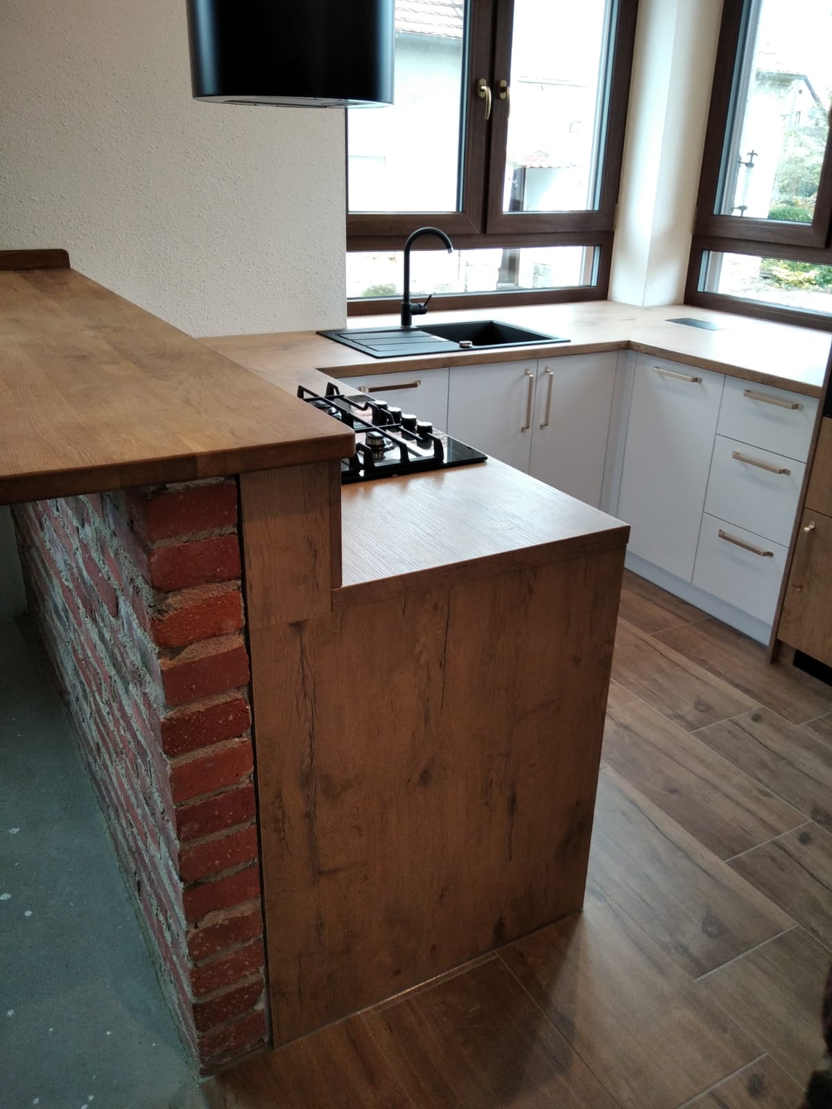 Jasna kuchenna zabudowa z wyspą i blatem drewnopodobnym.